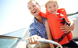 Father and son laughing while riding in a speedboat. We'll help you get out on the water or on the road with boat & RV loans!