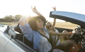 Two young women driving in their new convertible car, with the top down, singing and enjoying themselves.