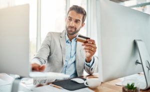 Businessman sits in his office ready to use his credit card to make an online purchase.