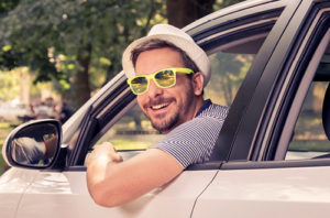 Man with yellow-rim sunglasses leans out of car window and smiles.