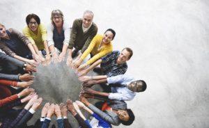 Diverse group of smiling people stand in a circle extending their hands towards the center.