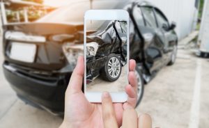 Smart phone held in hand taking photo of damaged vehicle. Get auto and home insurance through our partner, TruStage.
