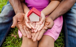 Daughter's hands holding a small house model, laying within her father's hands.