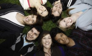 Diverse Group of Young Adults lay in a Circle, smiling on the Grass.