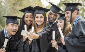 Group of college students take a smiling selfie together after graduation