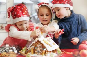Three young children decorate a gingerbread house.