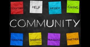 Blackboard with Community written on it has various colors of post-it notes spelling together, help, money, giving, teamwork, sharing, humanity, & partner