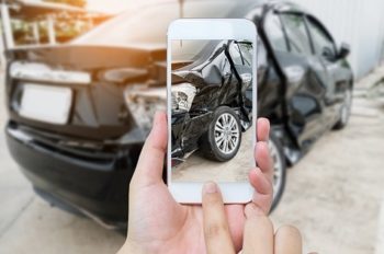 Smart phone held in hand taking photo of damaged vehicle. Get auto and home insurance through our partner, TruStage.