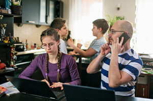 Photograph of man and woman working remotely from home with children playing in background
