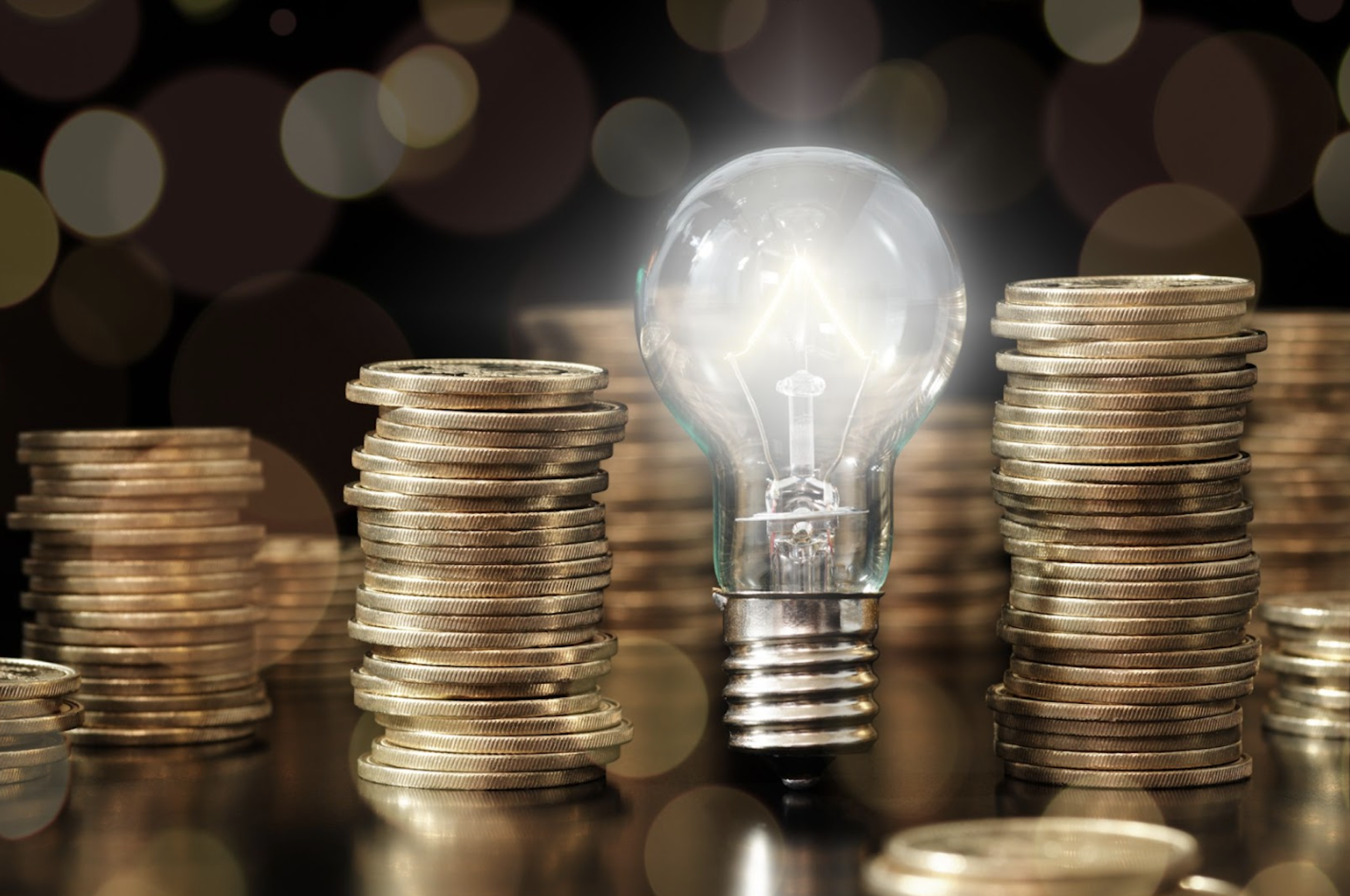 A lightbulb shining bright next to stacks of coins