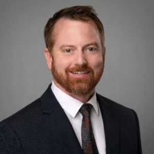 A headshot of Jesse Leavitt, a man wearing a blue suit and tie.
