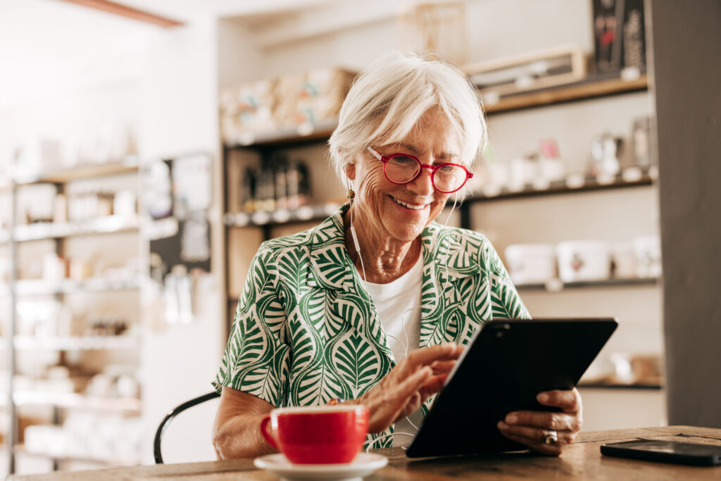 An older women sitting with a cup of coffee looking at a tablet